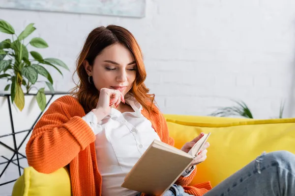 Focalisé femme lecture livre sur canapé jaune à la maison — Photo de stock