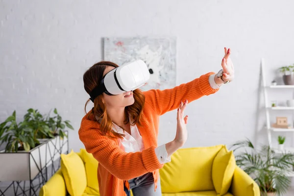 Junge Frau im vr-Headset gestikuliert mit ausgestreckten Händen beim Spielen im Wohnzimmer — Stockfoto