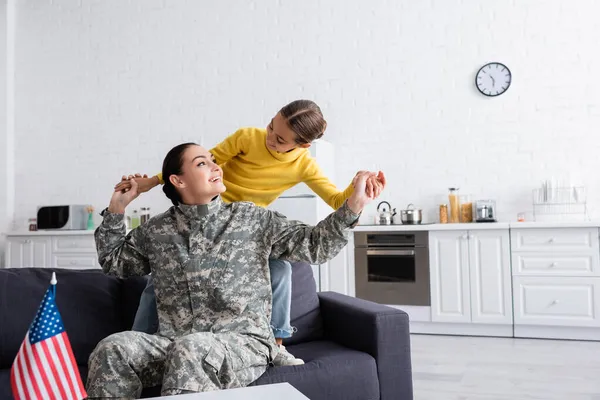 Kid de mãos dadas de mãe em uniforme militar perto da bandeira americana em casa — Fotografia de Stock