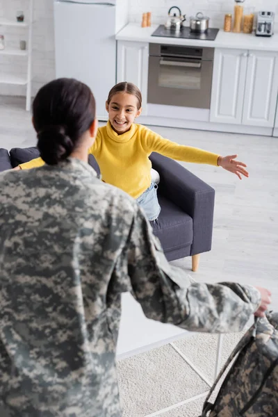 Preteen criança sorrindo para mãe turva em uniforme militar em casa — Fotografia de Stock