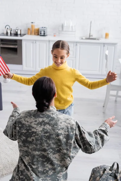 Woman in military uniform near smiling kid and backpack at home — Stock Photo