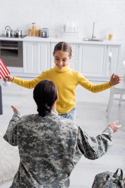 Donna in uniforme militare vicino sorridente bambino e zaino a casa — Foto stock