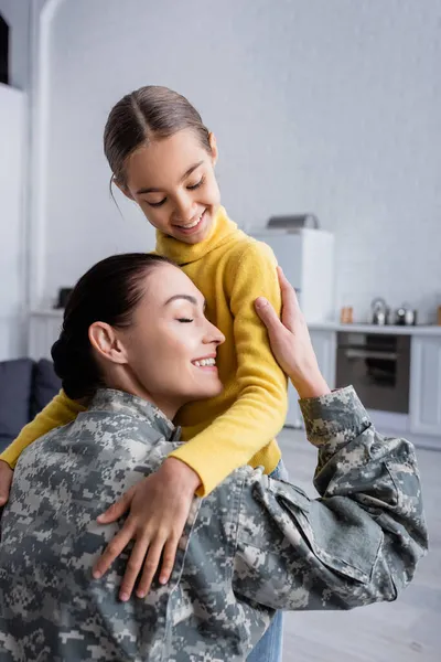 Mãe de uniforme militar abraçando filha em casa — Fotografia de Stock