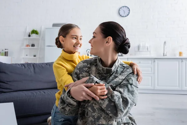 Sonriente niño abrazando mamá en uniforme militar en casa - foto de stock