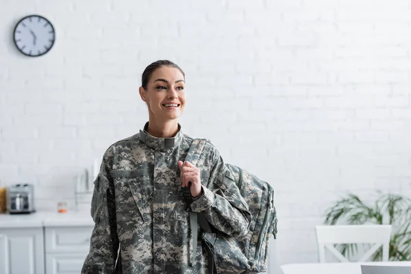 Веселая женщина в военной форме держит рюкзак дома — стоковое фото
