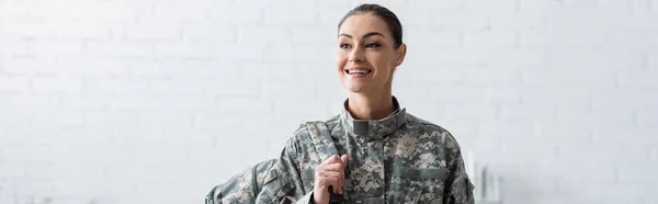 Soldado sorridente em uniforme militar segurando mochila em casa, banner — Fotografia de Stock