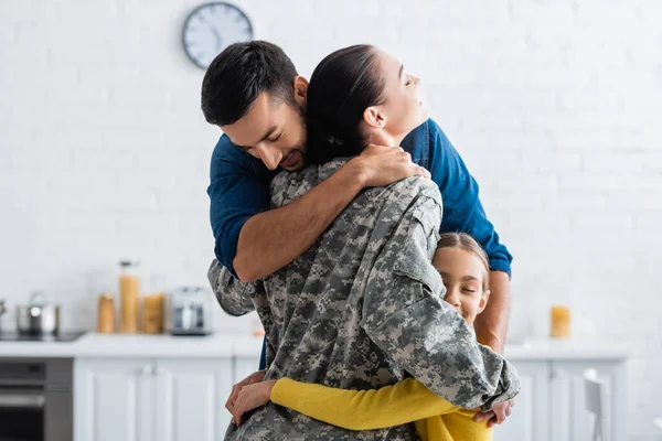 Чоловік і дочка обіймають матір у військовій формі на кухні — стокове фото