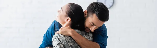 Mann umarmt Ehefrau in Militäruniform zu Hause, Banner — Stockfoto