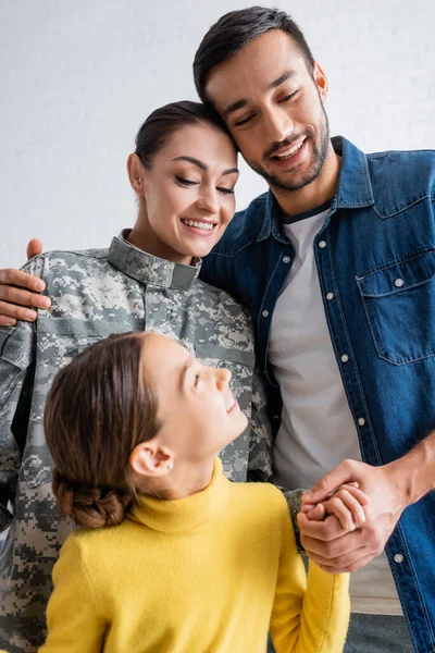 Smiling man holding hand of child and hugging wife in military uniform at home — Stock Photo