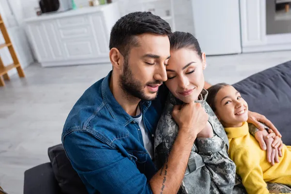 Man embracing wife in military uniform near child on couch at home — Stock Photo