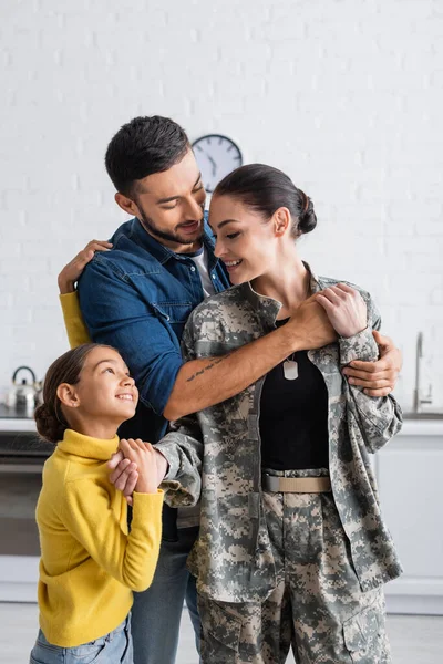 Uomo e bambino abbracciare donna in uniforme camuffamento a casa — Foto stock
