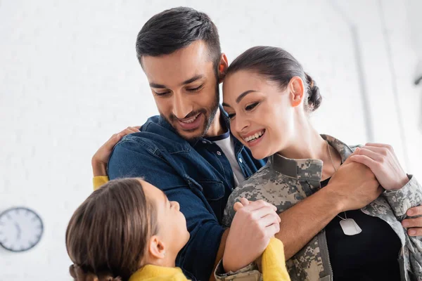 Un homme positif étreignant sa femme en uniforme militaire près d'une fille préadolescente à la maison — Photo de stock