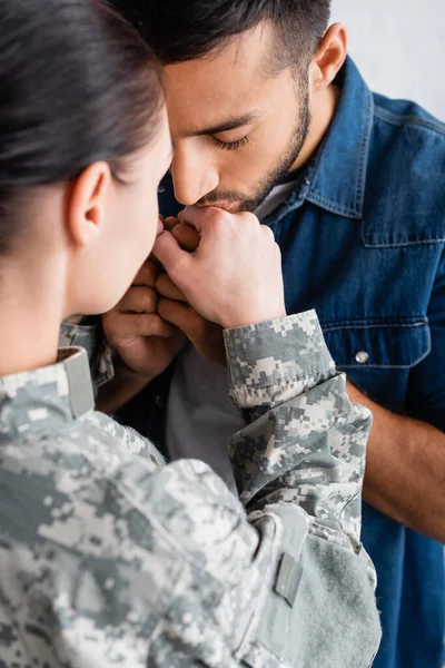 Hombre besando la mano de la esposa en uniforme militar en casa - foto de stock