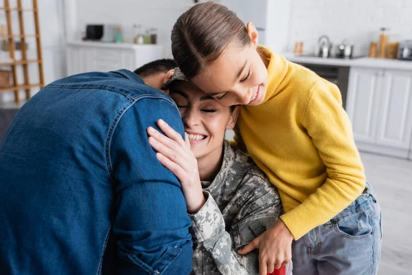 Sorrindo mulher em uniforme militar abraçando marido perto de filha pré-adolescente em casa — Fotografia de Stock