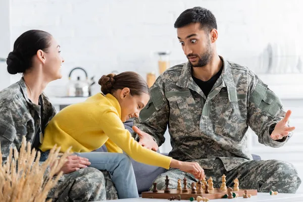 Homme étonnant en uniforme de camouflage jouant aux échecs avec la famille à la maison — Photo de stock