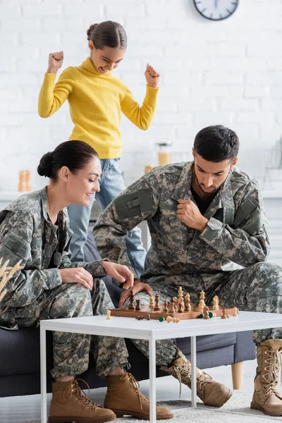Parents in military uniform playing chess near daughter at home — Stock Photo