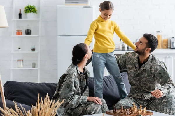 Felice genitori in uniforme camuffamento guardando preteen ragazza vicino a scacchi a casa — Foto stock