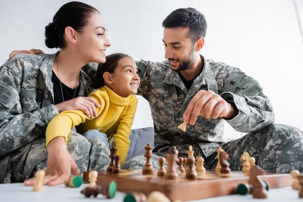 Homme heureux en uniforme militaire tenant une figure d'échecs près de sa fille et de sa femme à la maison — Photo de stock