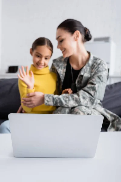 Laptop near blurred mother in military uniform and kid during video call at home — Stock Photo