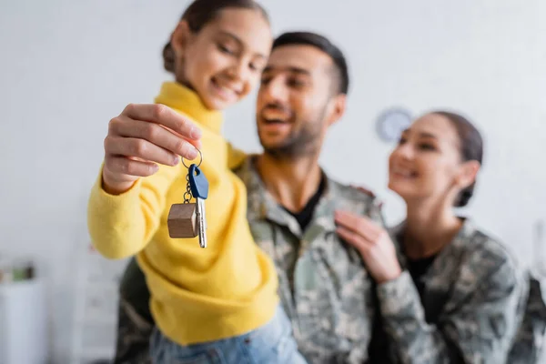 Blurred parents in military uniform holding daughter with key at home — Stock Photo