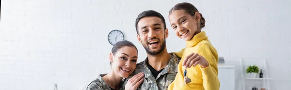 Happy family in military uniform holding daughter with key at home, banner — Stock Photo