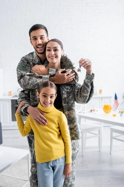 Smiling man in military uniform hugging wife with key near child at home — Stock Photo