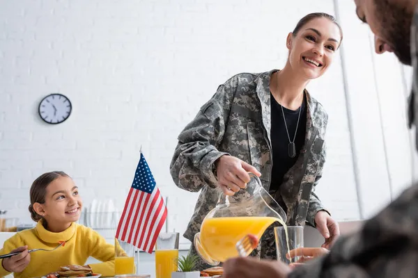 Smiling kid sitting near breakfast and smiling parents in military uniform at home — Stock Photo