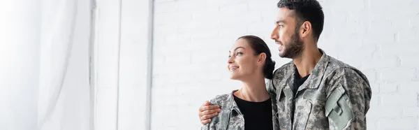 Husband in military uniform hugging wife at home, banner — Stock Photo