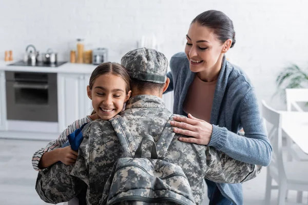 Sorrindo menina e mulher abraçando o homem em uniforme militar em casa — Fotografia de Stock