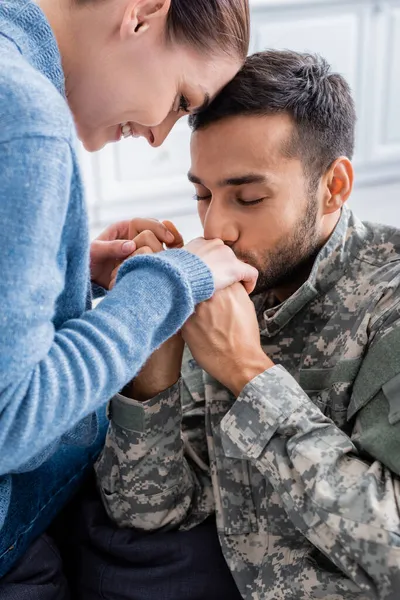 Homem de uniforme militar beijando mão de esposa sorridente em casa — Fotografia de Stock