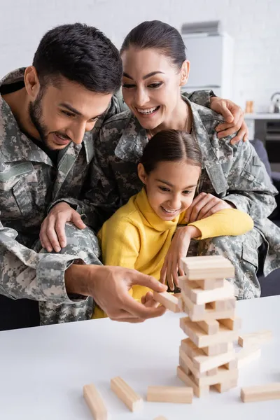 Parents positifs en camouflage jouant jeu de blocs de bois avec l'enfant à la maison — Photo de stock