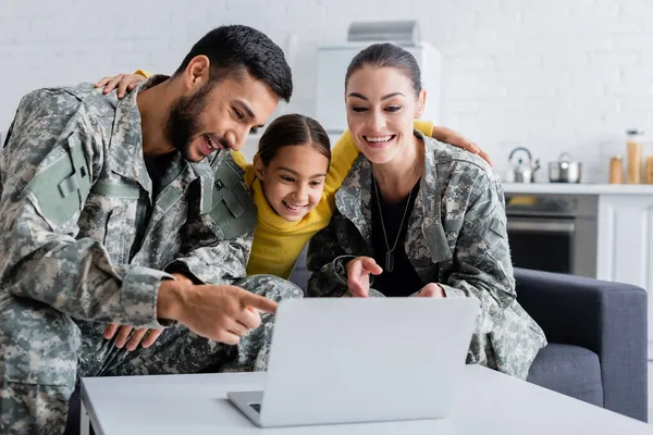 Smiling parents in camouflage looking at laptop near child at home — Stock Photo