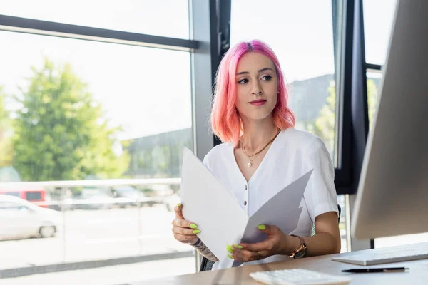 Femme d'affaires percée avec dossier de tenue de cheveux roses et regardant le moniteur d'ordinateur — Photo de stock