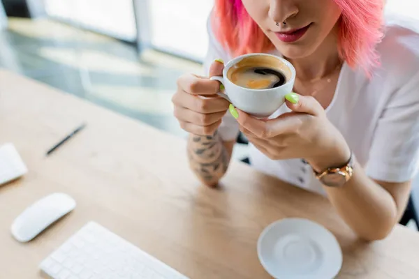 Vista cortada de gerente perfurado com cabelo rosa segurando xícara de café no escritório — Fotografia de Stock