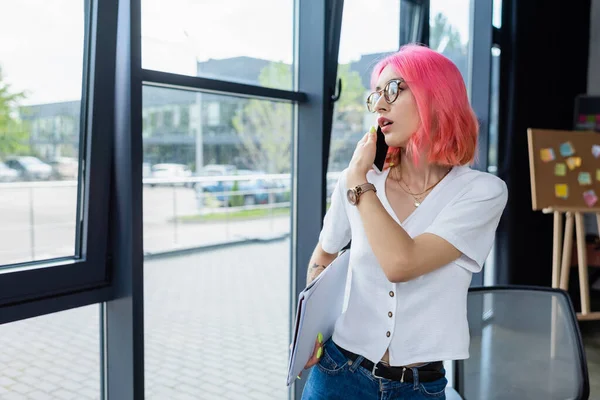 Pierced manager with pink hair talking on cellphone near windows — Stock Photo