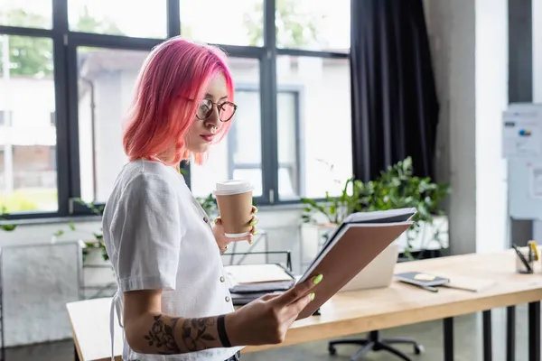 Jovem gerente com cabelo rosa segurando copo de papel e pastas — Fotografia de Stock