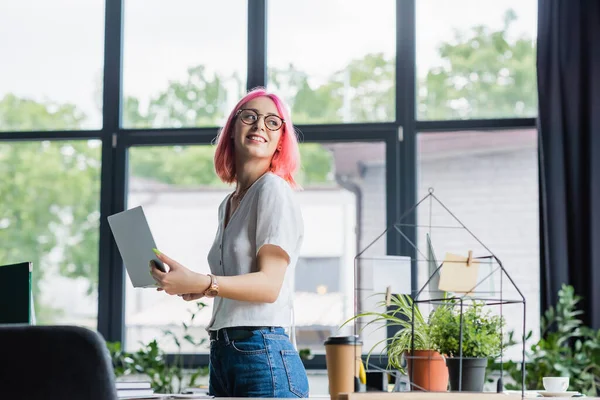 Jovem empresária alegre com cabelo rosa usando laptop no escritório — Fotografia de Stock