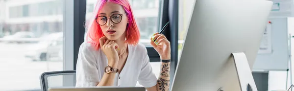 Gepiercte Geschäftsfrau mit pinkfarbenen Haaren hält Stift in der Nähe des Computermonitors, Banner — Stockfoto