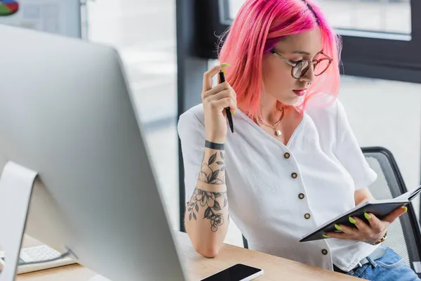 Mujer de negocios tatuada con el pelo rosa que sostiene la pluma y el cuaderno - foto de stock