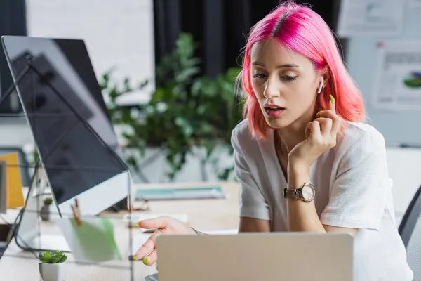 Mujer de negocios perforada con cabello rosa en auriculares mirando el portátil - foto de stock