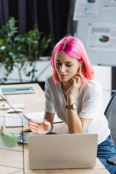 Femme d'affaires percée avec des cheveux roses ajustant écouteur tout en regardant ordinateur portable — Photo de stock