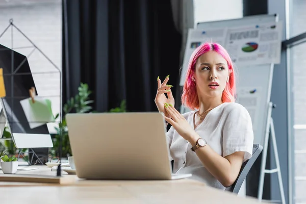 Проколота бізнес-леді в навушниках жестикулює біля ноутбука — стокове фото