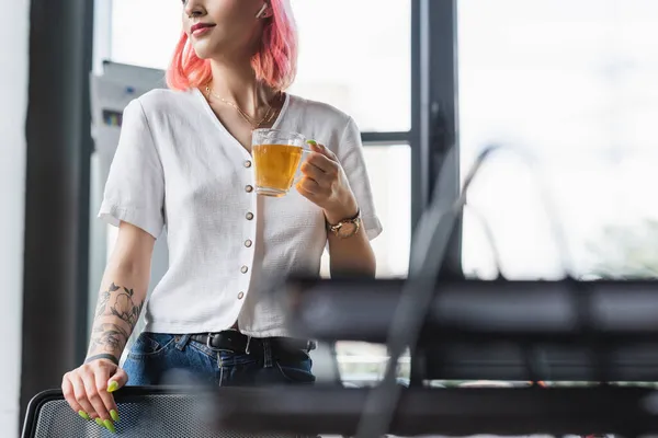 Abgeschnittene Ansicht einer fröhlichen Geschäftsfrau mit rosa Haaren und Kopfhörer, die eine Tasse Tee im Büro hält — Stockfoto