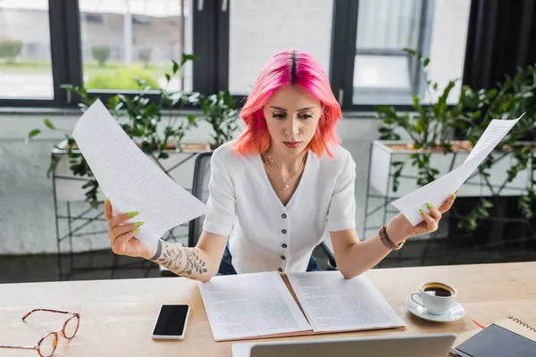 Busy businesswoman with colorful hair holding documents near devices on desk — Stock Photo
