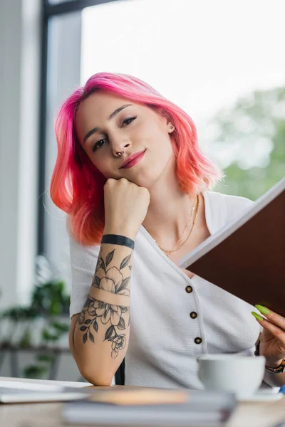 Улыбающаяся деловая женщина с розовыми волосами, держащая папку в офисе — стоковое фото