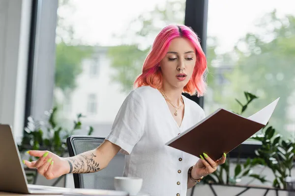 Mujer de negocios disgustada con carpeta de celebración de pelo rosa en la oficina - foto de stock