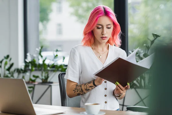 Занятая деловая женщина с розовыми волосами, держащая папку в офисе — стоковое фото