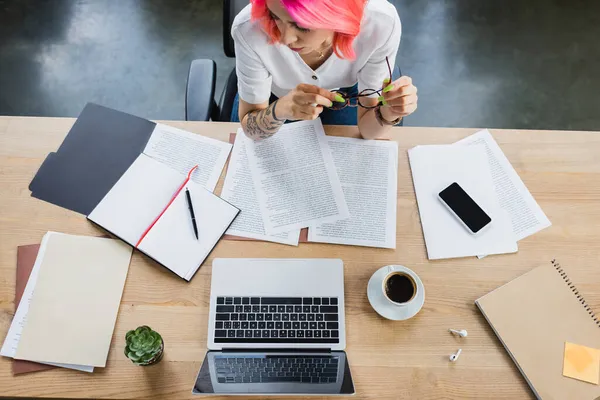 Vista superior de mujer de negocios con pelo rosa con gafas cerca de documentos y gadgets en el escritorio - foto de stock