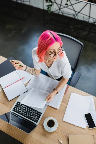 Vue du dessus de femme d'affaires heureuse avec des cheveux roses tenant stylo près des documents et des appareils sur le bureau — Photo de stock