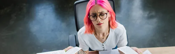 Вид зверху втомленої бізнес-леді з рожевим волоссям, що тримає документи в офісі, банер — стокове фото